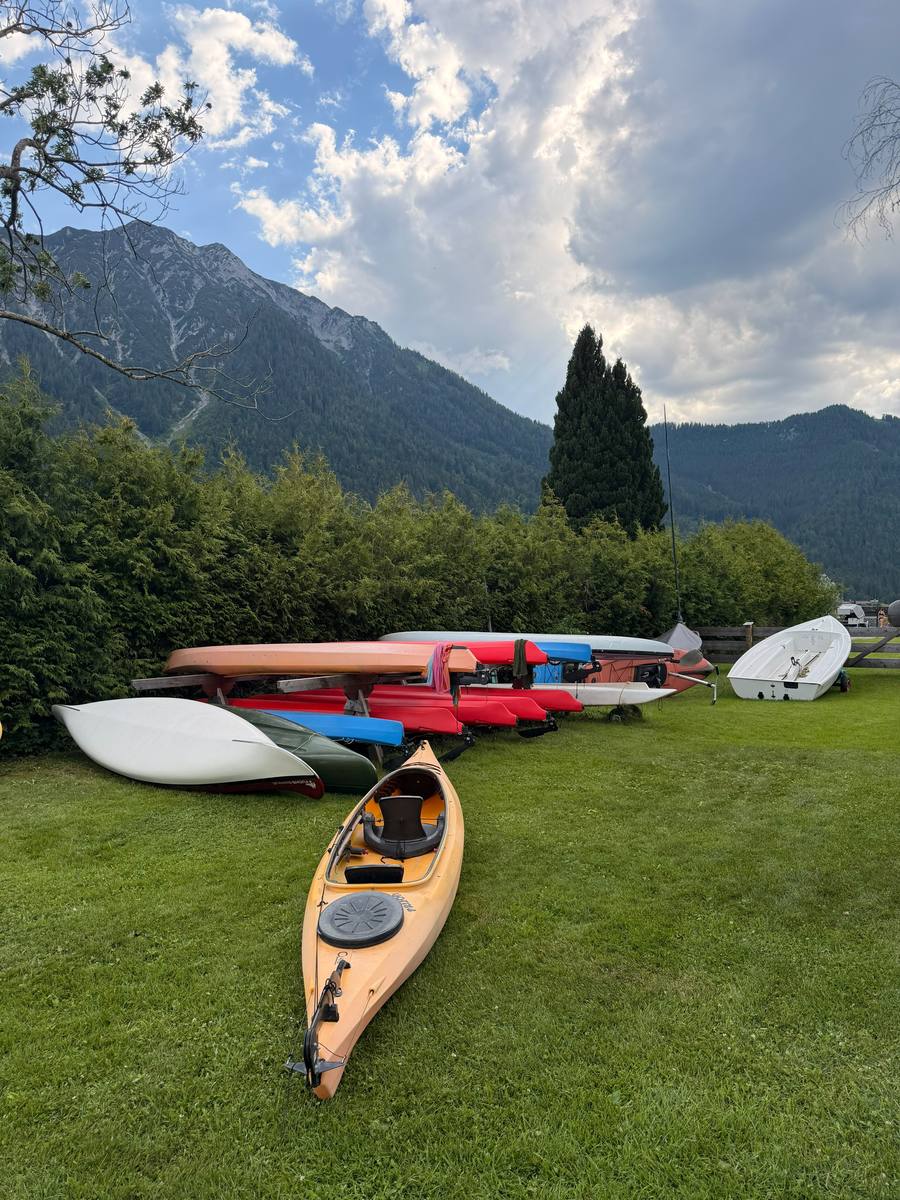 Gelbes Kajak auf der Wiese, dahinter weitere Boote und Berge