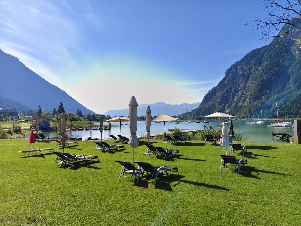 Liegestühle und Sonnenschirme am Morgen auf der Seewiese, dahinter der ruhige Achensee