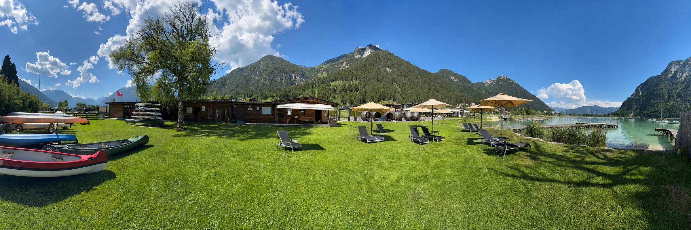 Panorama der Seewiese: Kanadier, Station und Liegestühle mit Schirmen am Achensee